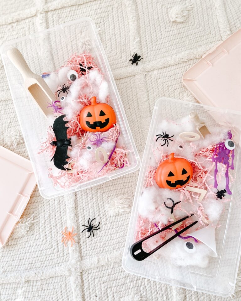 Halloween sensory activity bin for toddlers and preschoolers. Bins contain pink paper shred, pumpkin sensory ball, spiders, bats and bugs. Tongs and scoops for sorting.