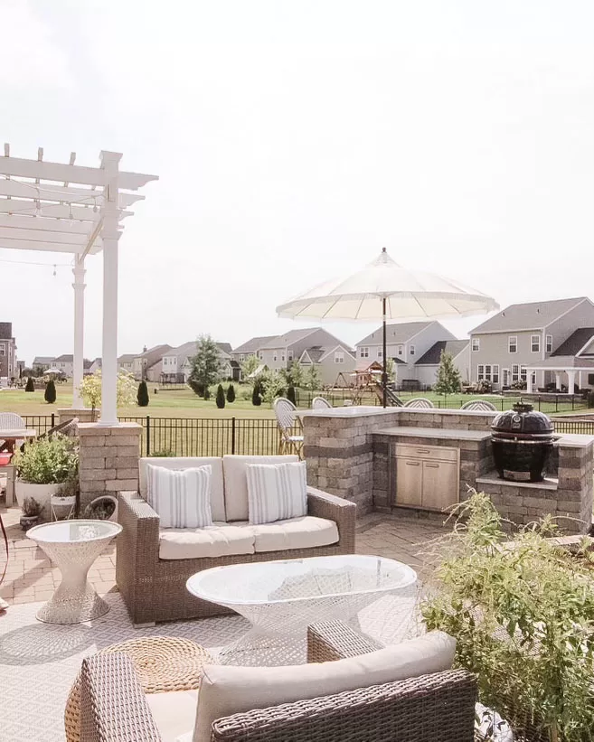 a backyard oasis complete with an outdoor kitchen, bar, and grill, alongside a paved patio area adorned with a parasol umbrella