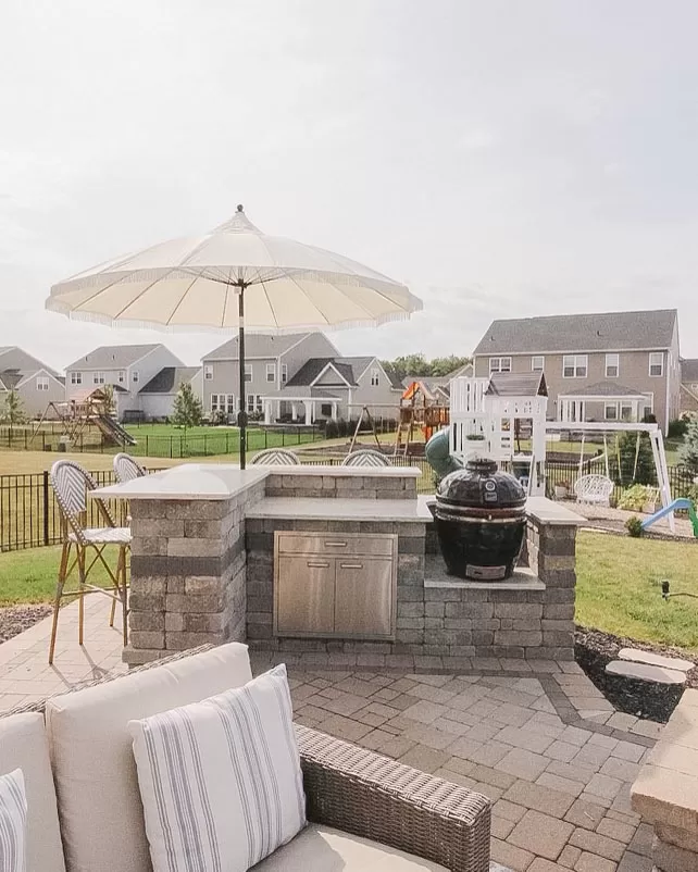 A backyard oasis complete with an outdoor kitchen, bar, and grill, alongside a paved patio area adorned with a parasol umbrella