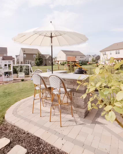 outdoor kitchen with white parasol umbrella, bamboo counter stools, patio and pergola ambiance, suburban backyard, outdoor bar and grill with granite countertops