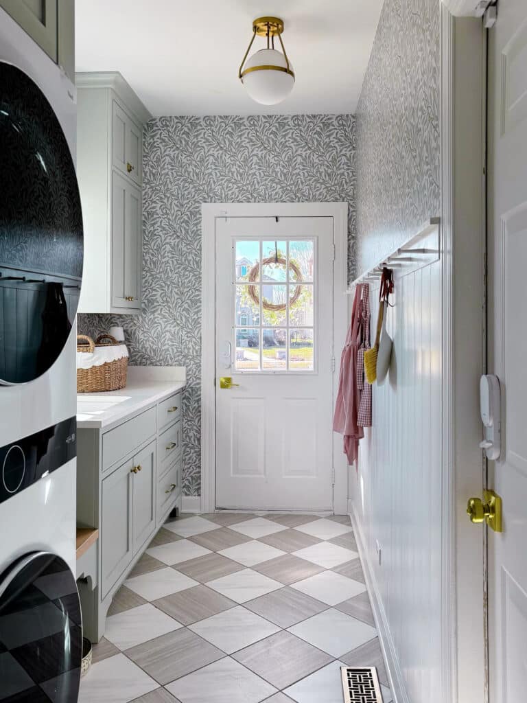 Green laundry room with checkered floor and botanical print wallpaper, laundry room ideas with stacked washer and dryer, laundry room ideas stacked, remodeled laundry room, Checkered floor tile, checkered floor, ceramic checkered floor, inset cabinets, green cabinetry, sherwin williams comfort gray